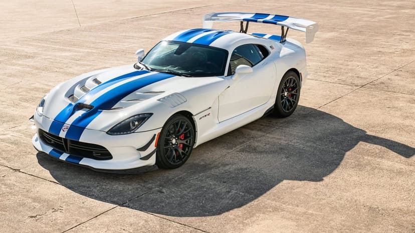 White Dodge Viper GTS-R with blue racing stripes and a large wing parked on a concrete surface under bright light.
