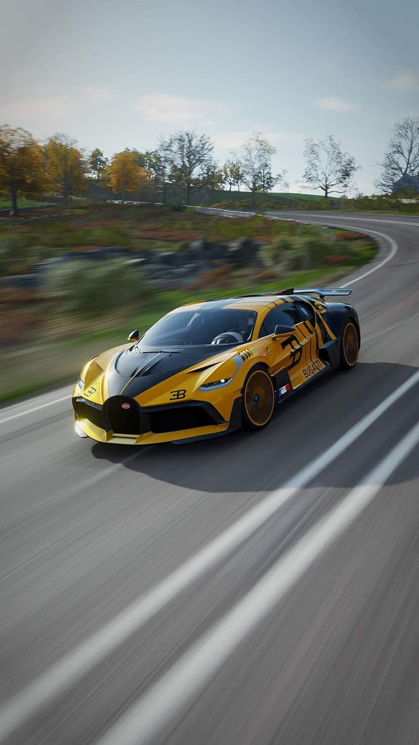 Bugatti Divo hypercar racing on a curved asphalt road with orange autumn trees and a clear blue sky background.
