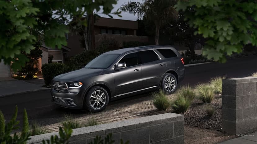 Charcoal Dodge Durango SUV parked on a paved driveway at dusk surrounded by suburban greenery and low walls.