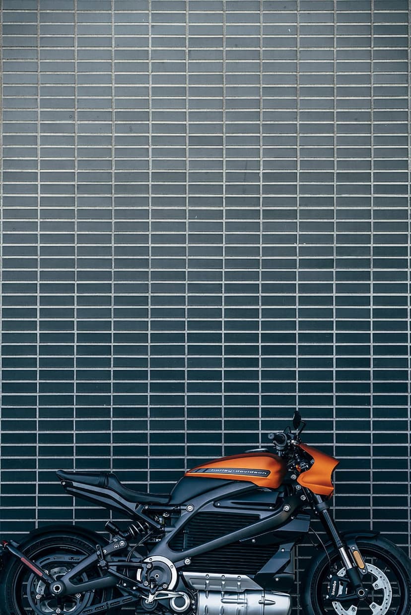 Orange Harley-Davidson LiveWire electric motorcycle parked against a dark textured brick wall in an urban setting.