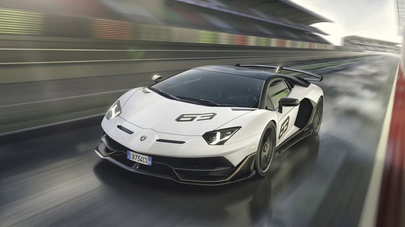 White Lamborghini Aventador SVJ 63 racing on a wet track with motion blur and grandstands in the background.