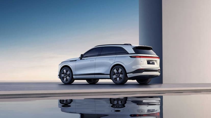 White electric SUV parked next to a minimalist grey wall with a sharp reflection in a still pool of water.
