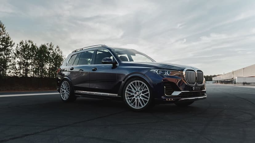 Dark blue BMW X7 SUV with silver multi-spoke wheels parked on an asphalt lot under a cloudy sky.