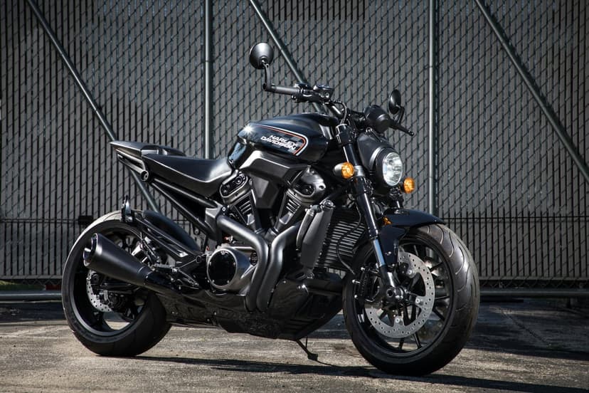 Black Harley Davidson motorcycle with a muscular engine parked against a textured grey industrial metal fence.