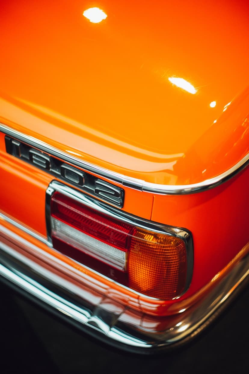 BMW 2002 rear taillight featuring chrome housing and a numerical emblem on glossy orange metallic paintwork.