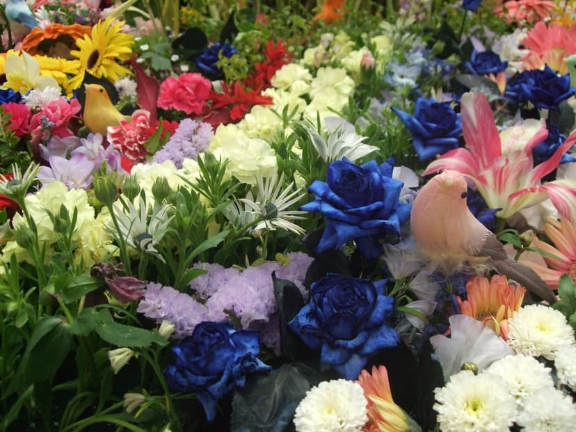 Two decorative birds rest inside a dense bouquet of multicolored silk flowers with realistic petals and leaves.