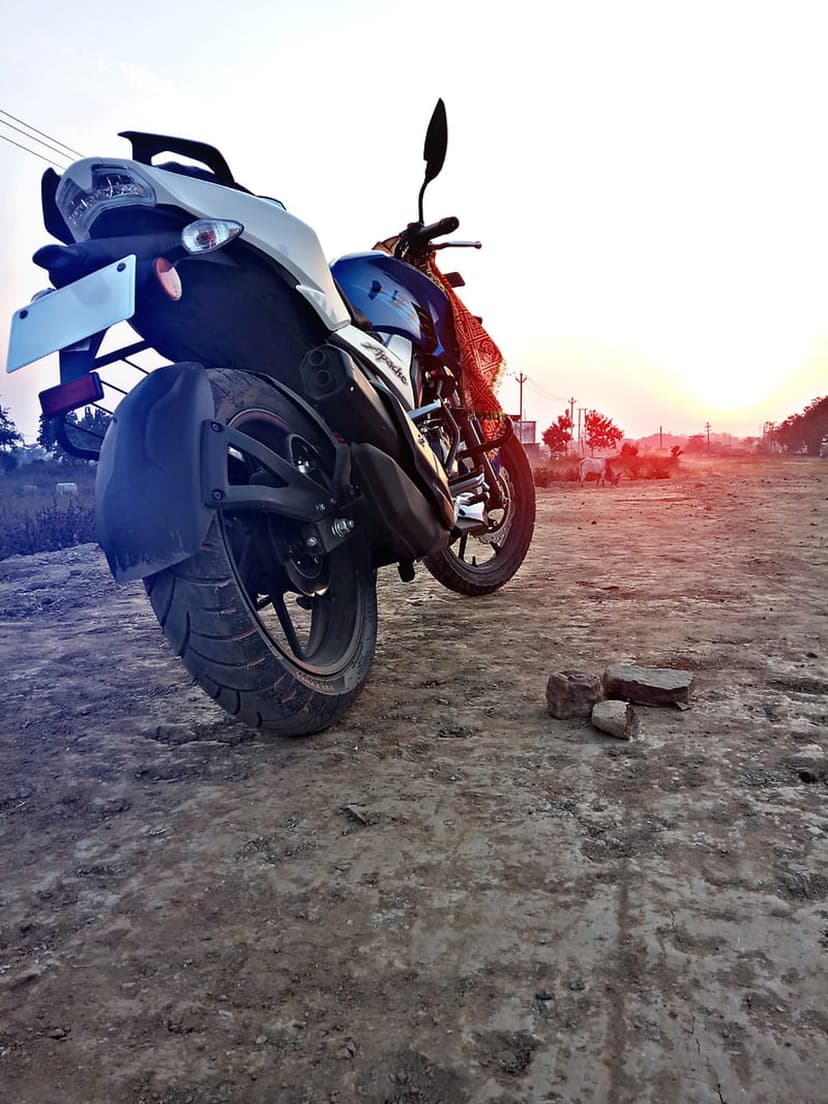 Blue motorcycle on a dirt road at sunset with a red cloth on the bars and golden light on the rear tire.