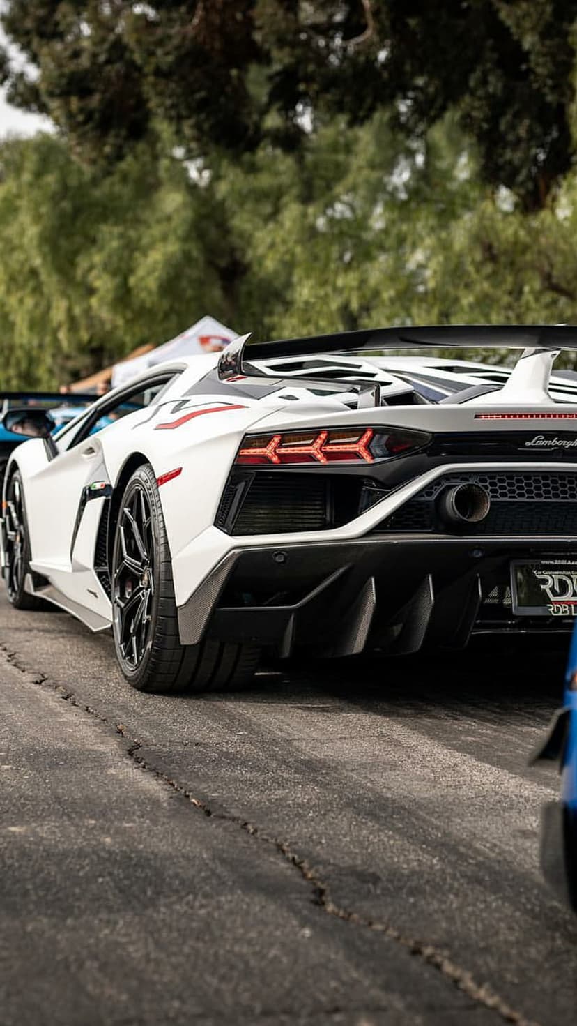 Lamborghini Aventador SVJ in white features a massive rear wing and sharp taillights on cracked asphalt by trees.