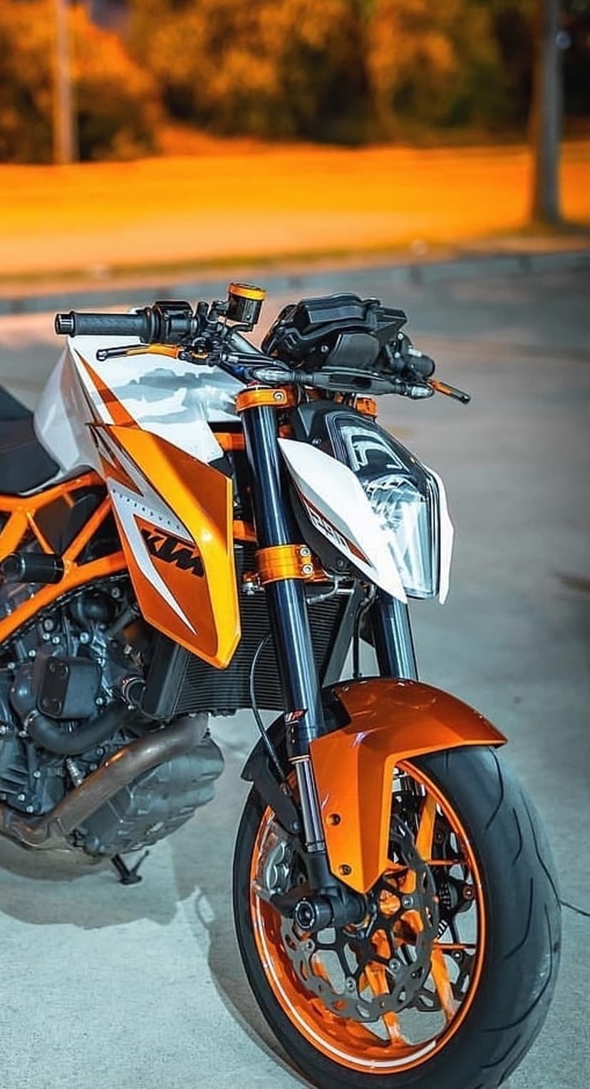 KTM motorcycle front view with orange fairings, anodized forks, and detailed brake system against a blurred background.
