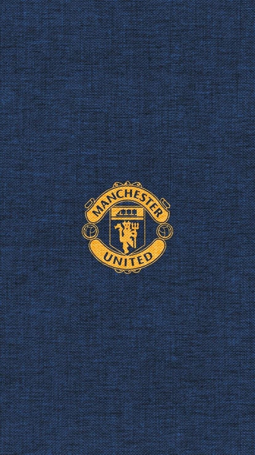 Manchester United crest in gold metallic finish centered on a dark blue textured fabric soccer jersey background.
