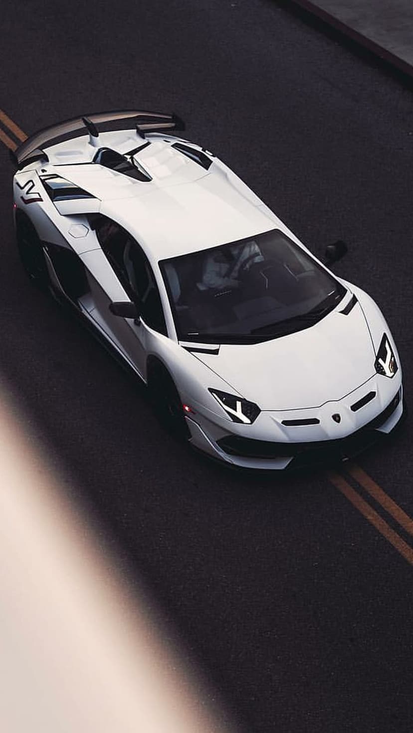 White Lamborghini Aventador SVJ parked on dark asphalt with yellow lane markings viewed from an overhead angle.