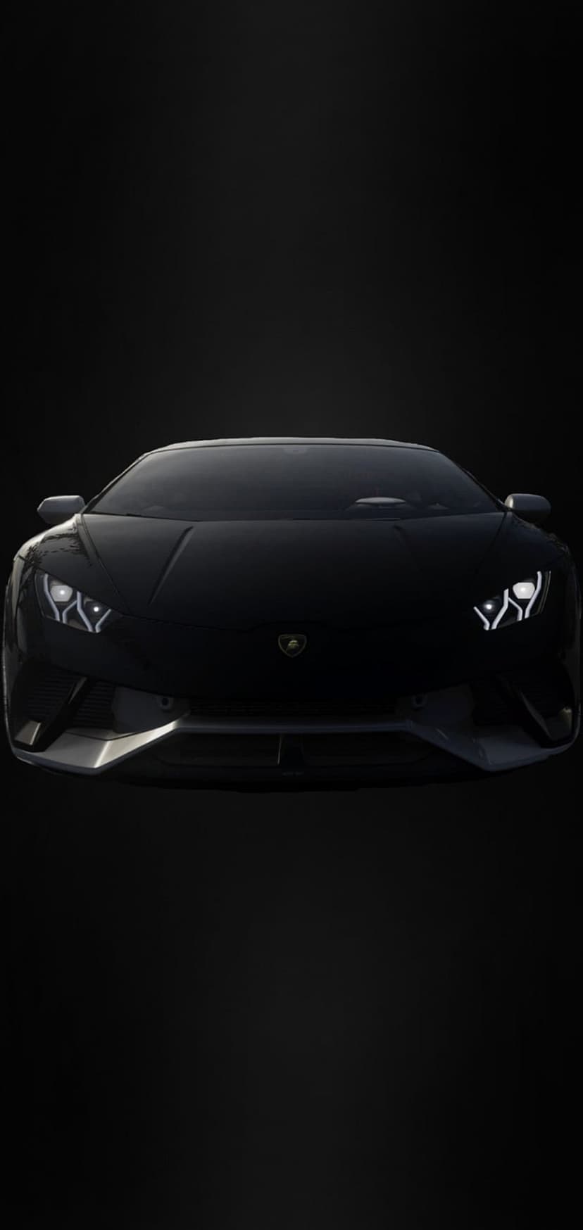 Black Lamborghini supercar with bright white LED headlights viewed from a low front angle on a dark backdrop.