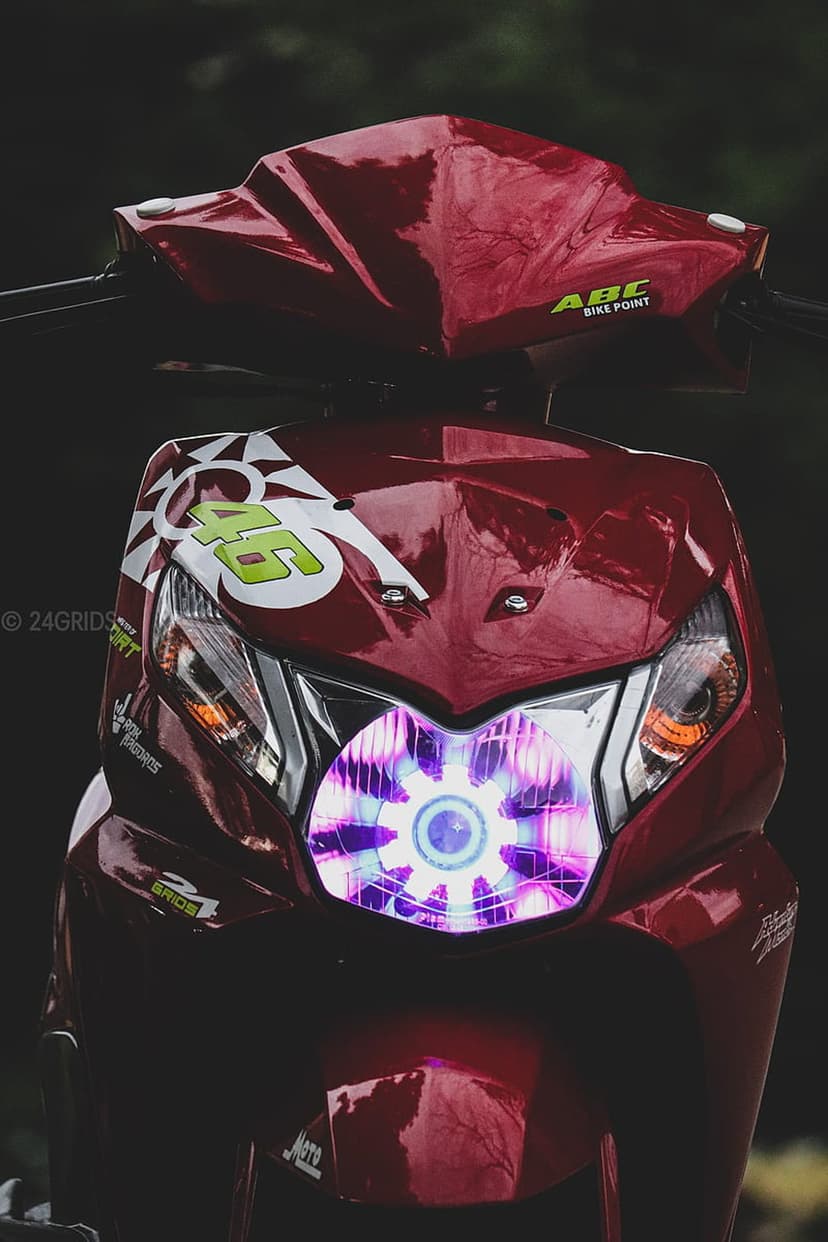 Red scooter with a multi-colored LED headlight and racing decals shown against a dark blurred background.