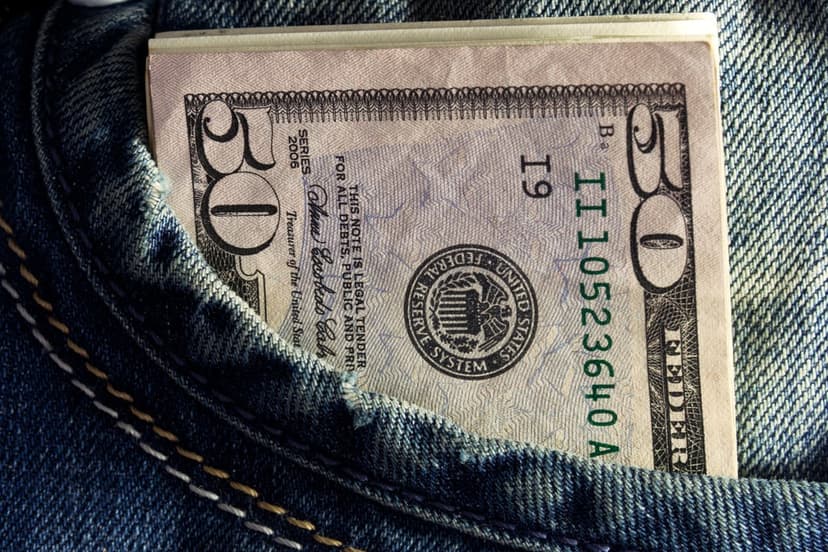 Fifty dollar bill with Ulysses S. Grant portrait partially tucked into the front pocket of blue denim jeans.