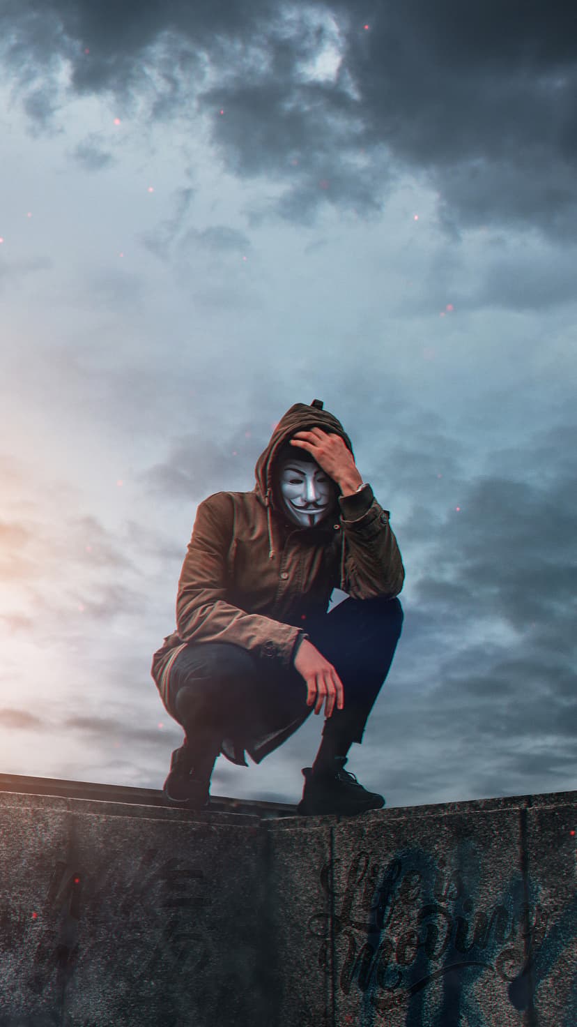 Masked street figure in a dark hood with glowing neon eyes stands against a blurred city background.