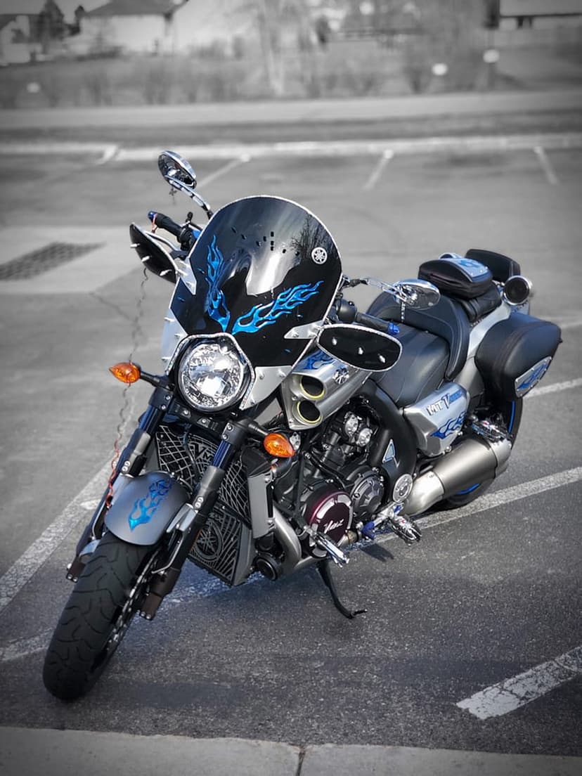Yamaha VMAX cruiser with blue flame decals on the fairing and black saddlebags in an asphalt parking area.