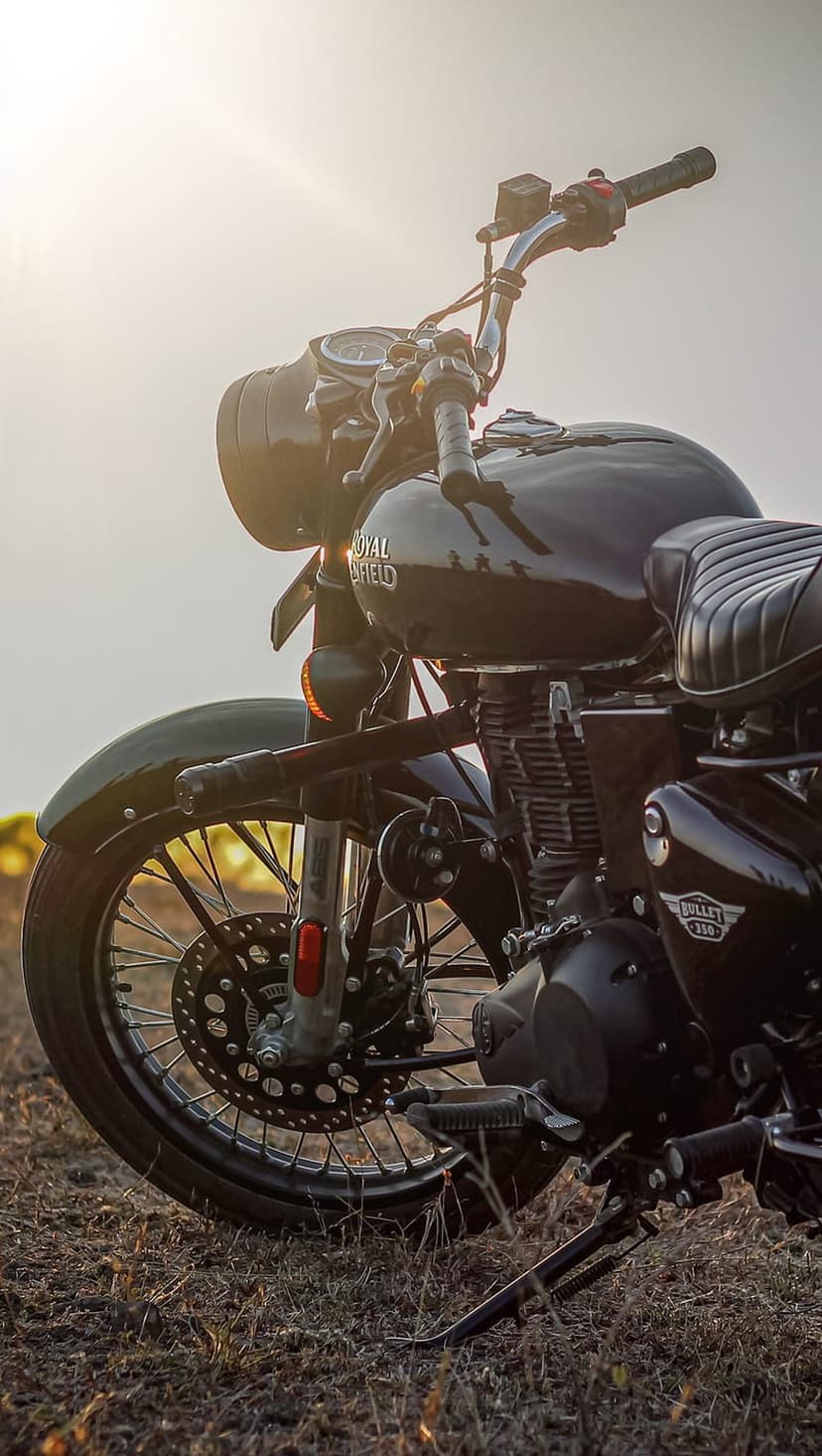 Royal Enfield Bullet 350 motorcycle with chrome handlebars and engine on dry grass under golden sunset light.