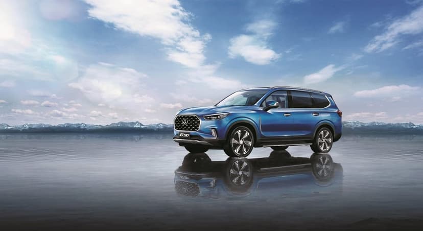Blue SUV parked on a reflective wet surface with snow-capped mountains under a bright blue cloudy sky.