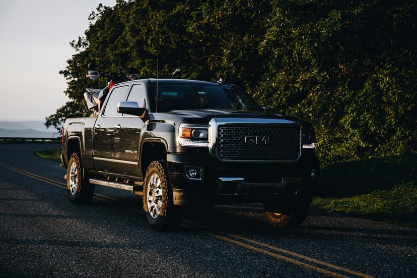 Black GMC Sierra pickup truck with chrome accents parked on a winding asphalt road during a vibrant golden sunset.