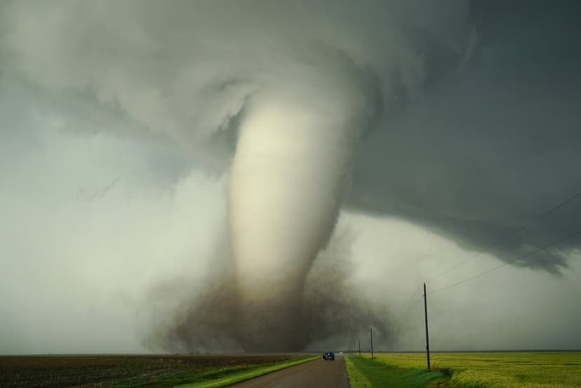 Massive dark tornado funnel touching down on a flat rural landscape with swirling debris under stormy skies.