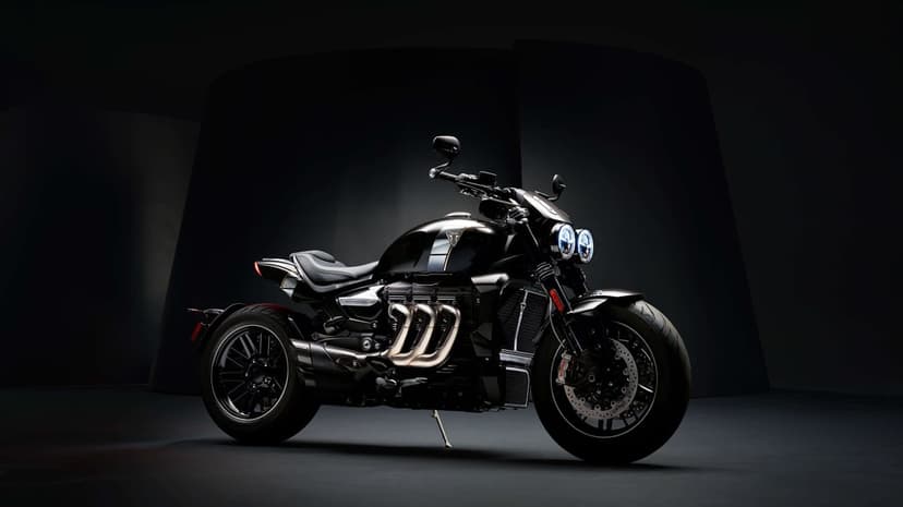 Triumph Rocket 3 motorcycle with chrome triple exhausts and twin LED headlights in a dark studio.