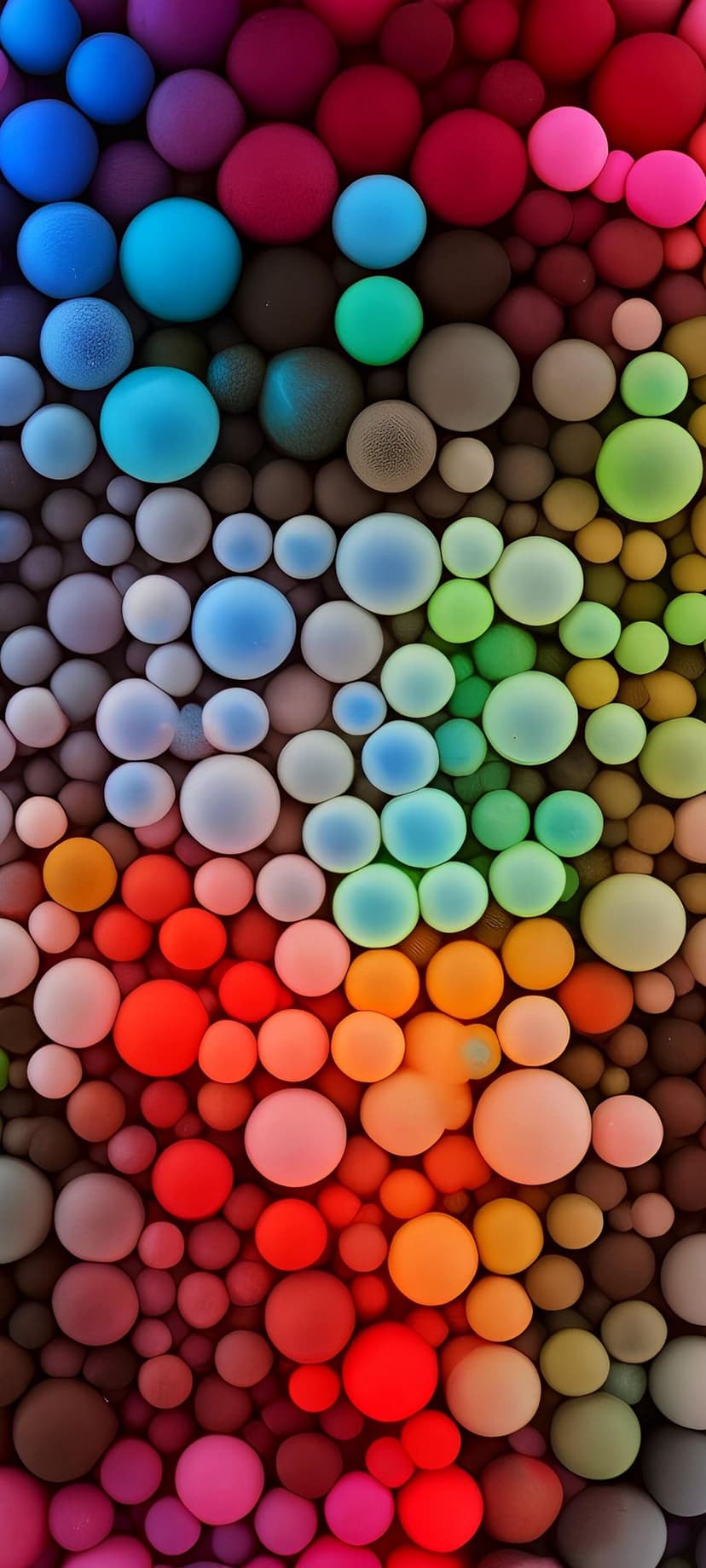 Multi-colored spheres in various sizes arranged in a vertical rainbow gradient with soft shadows and highlights.