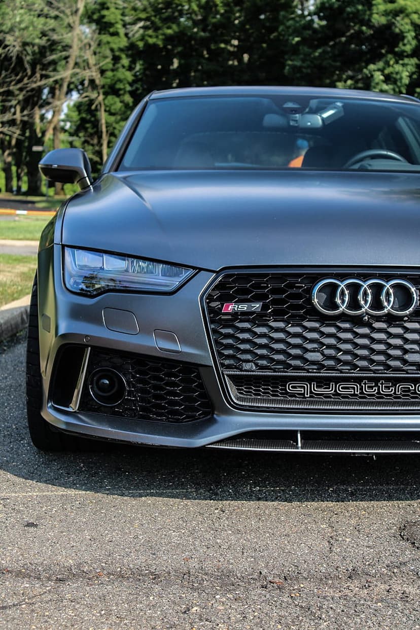 Audi RS7 front grille featuring a Quattro badge, honeycomb mesh, and LED headlights against green foliage background.