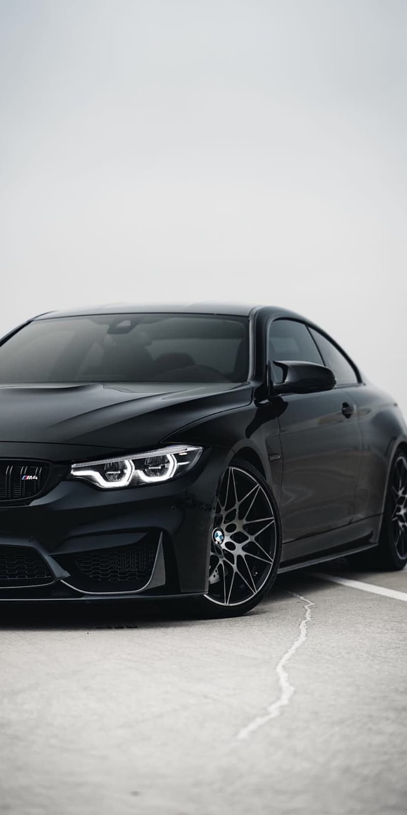 BMW M4 Coupe with illuminated headlights and alloy wheels parked against a dim, overcast sky background.