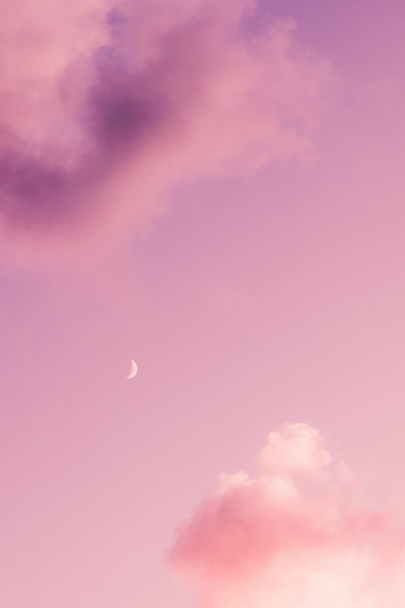 Slender silver crescent moon floats amidst soft magenta and violet wispy clouds against a darkening twilight sky.