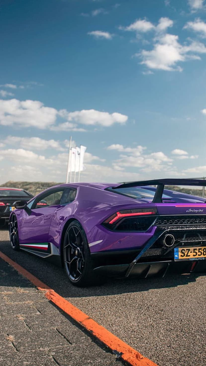 Purple Lamborghini Huracán with a rear spoiler on a sunny racetrack, showcasing a custom license plate.