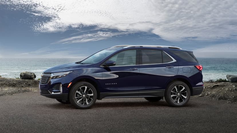 Dark blue Chevrolet Equinox SUV parked on a coastal road against a scenic ocean and cloudy sky background.