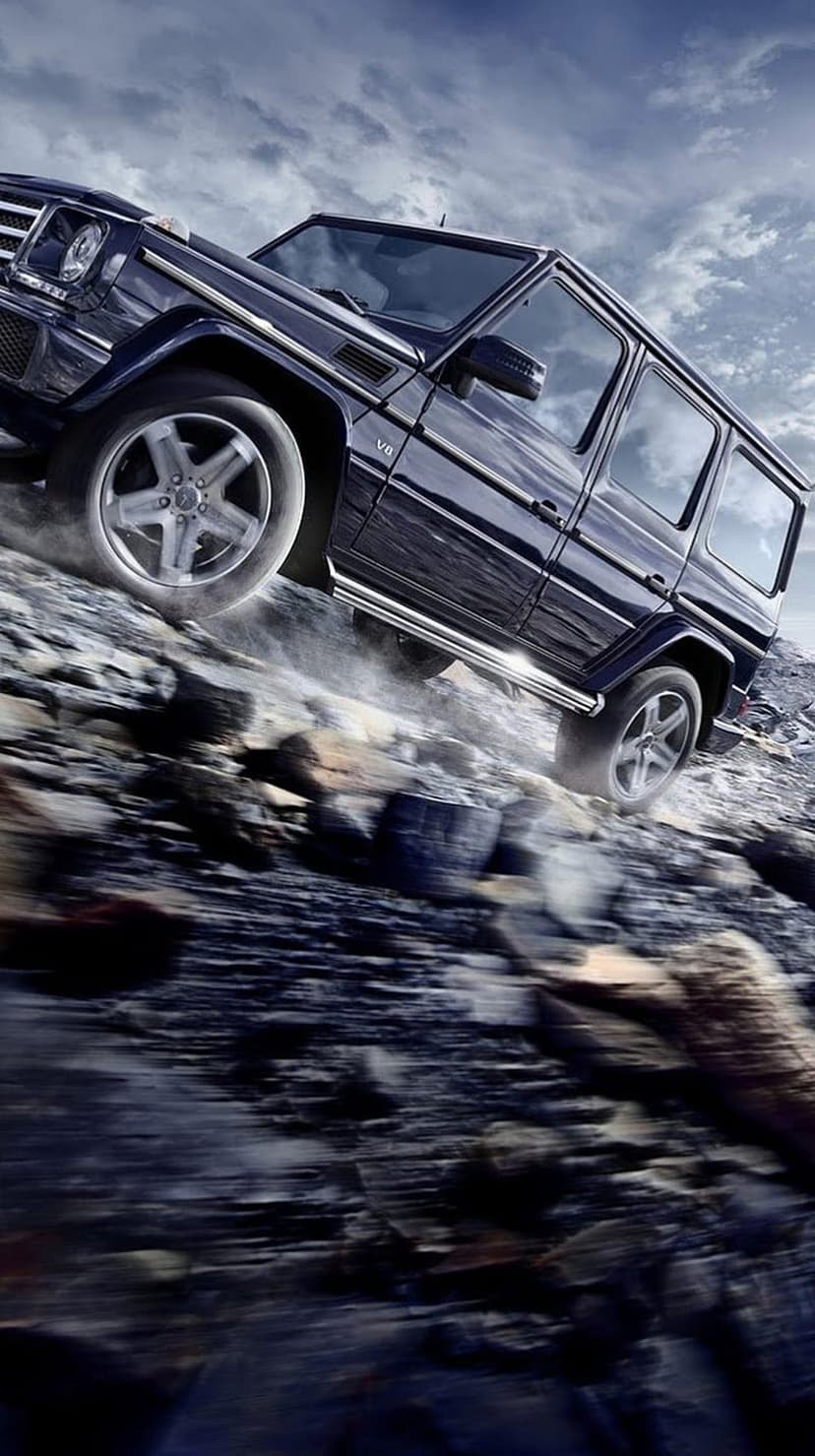 Mercedes G-Wagon climbs a steep rocky slope, kicking up thick dust against a dark, moody, atmospheric sky.