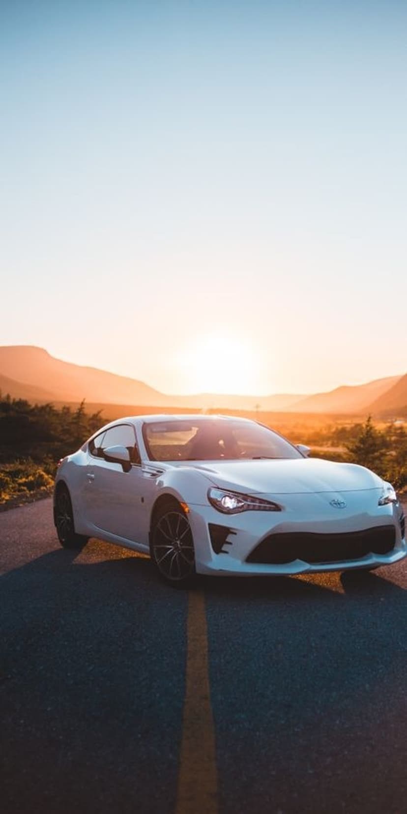 White Toyota 86 sports car parked on a mountain road at sunset with golden light hitting the vehicle body.