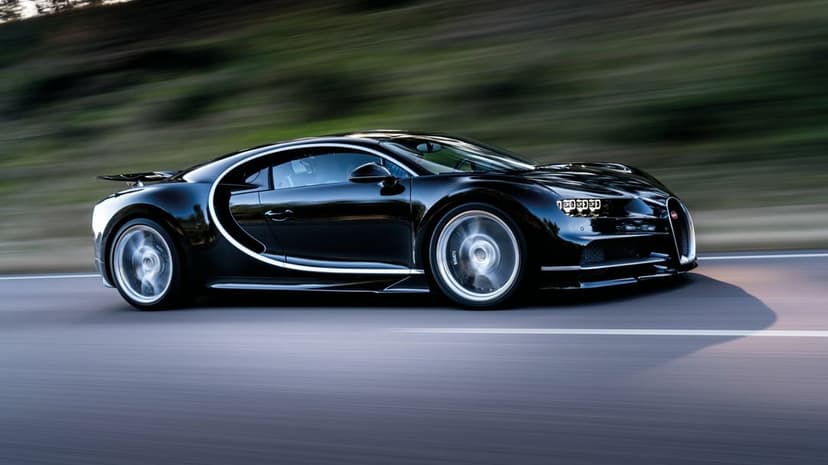 Black Bugatti Chiron hypercar in motion on a road with blurred background and spinning silver alloy wheels.