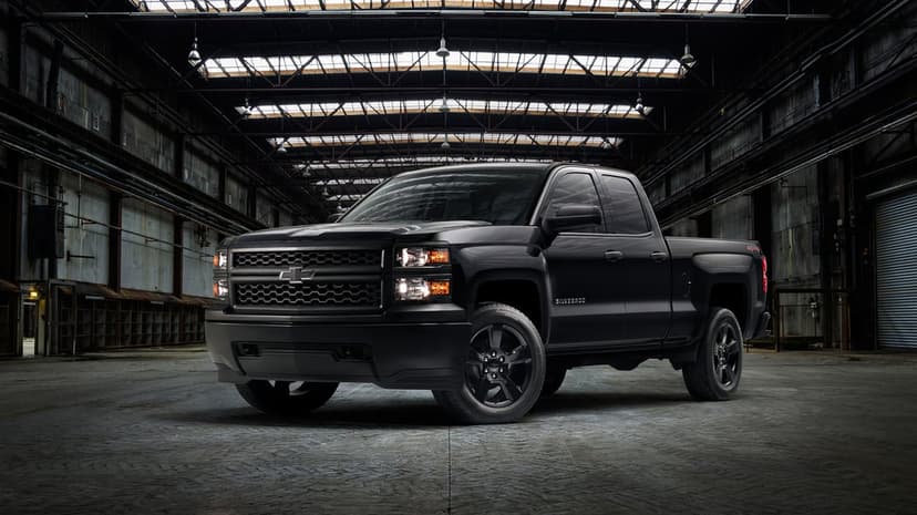 Black Chevrolet Silverado truck with amber lights glowing inside a dark, high-ceilinged industrial warehouse.