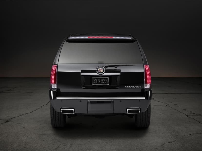 Rear view of a black Cadillac Escalade SUV with glowing red LED taillights on a cracked concrete floor.
