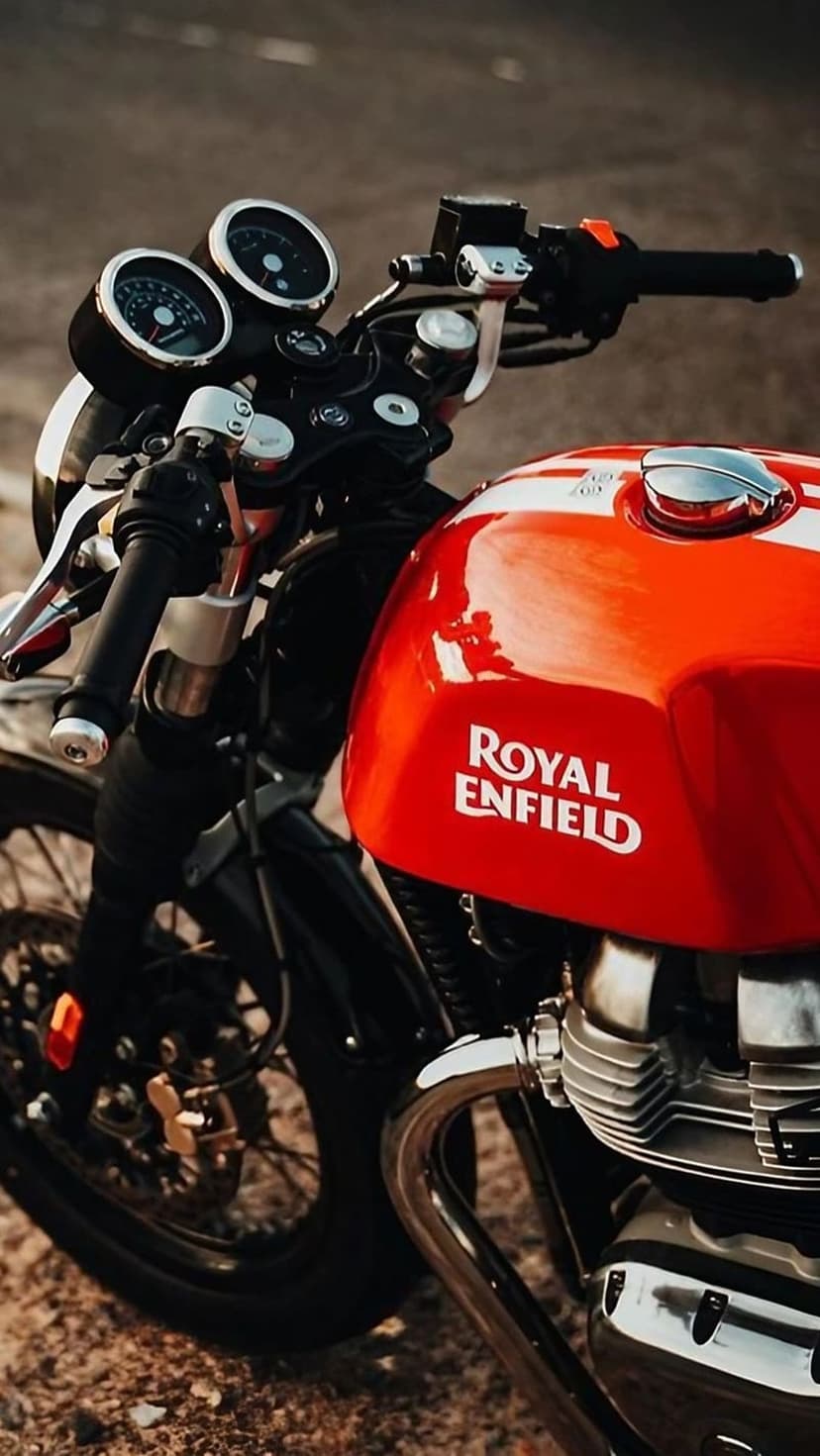 Red Royal Enfield motorcycle fuel tank with white pinstripes, chrome engine parts, and vintage analog gauges.