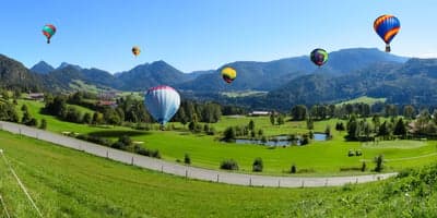 Vibrant Hot Air Balloons Over Alpine Green Valley Wallpaper