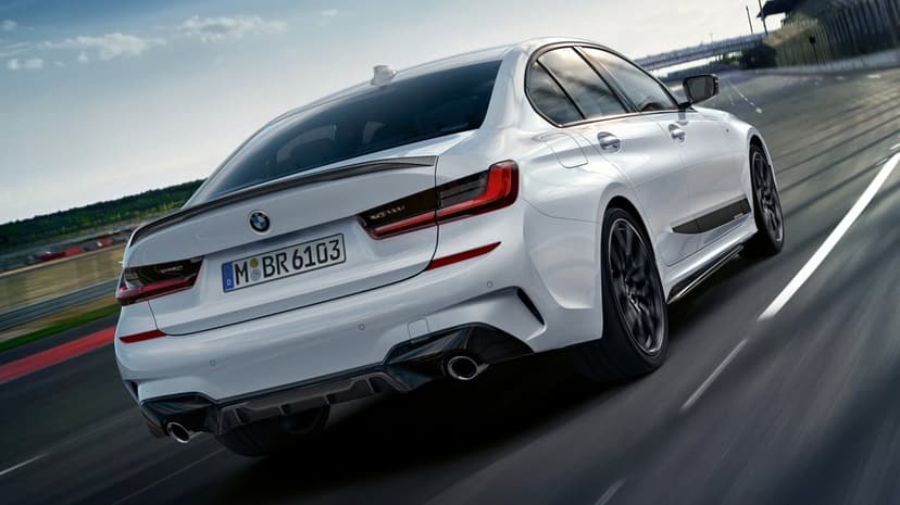 White luxury sport sedan speeding on a racetrack with visible carbon fiber spoiler and rear diffuser.