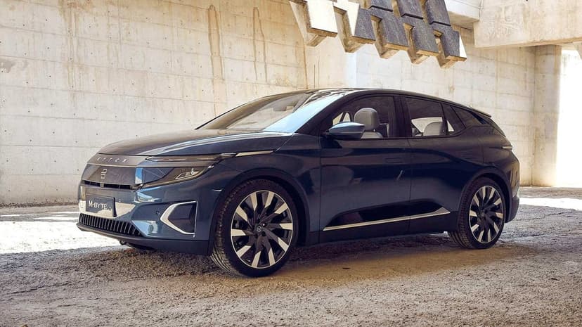 Byton M-Byte electric SUV in navy blue parked by concrete walls with sharp geometric shadows in bright daylight.