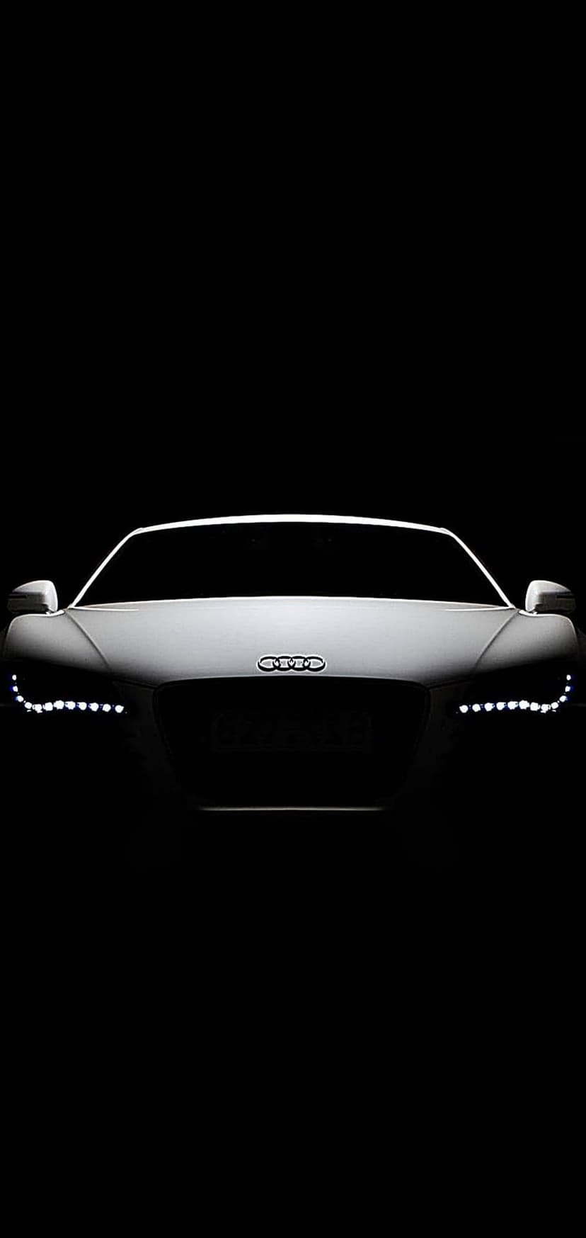 Audi R8 LED headlights and front grille illuminated against a dark black background in a vertical view.
