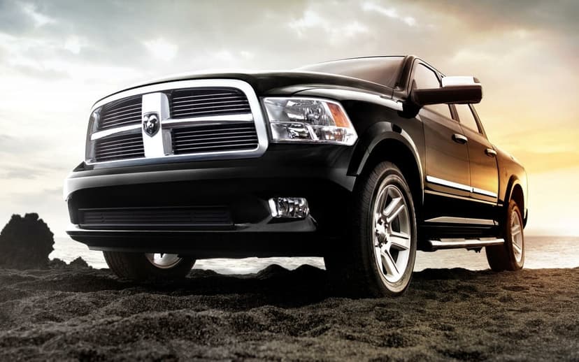 Black pickup truck with a chrome grille parked on a dark sandy beach under a dramatic golden hour sky.