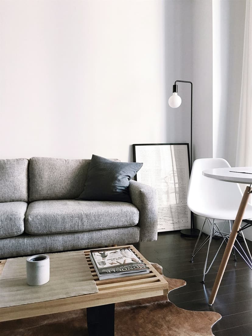 Gray fabric sofa and white molded chairs arranged in a bright minimalist living room with sheer window curtains.