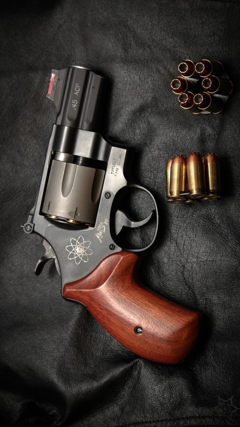 S&W .45 ACP revolver featuring wooden grips alongside brass bullets and a speedloader on a dark surface.