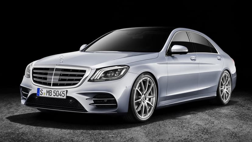 Silver Mercedes-Benz S-Class sedan parked on textured ground against a solid black studio background.