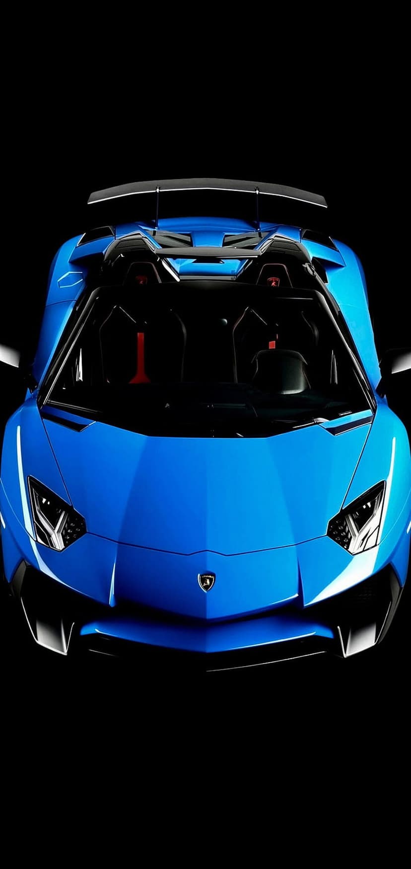 Blue Lamborghini Aventador SVJ Roadster showing sharp headlights and aerodynamic body on a dark background.