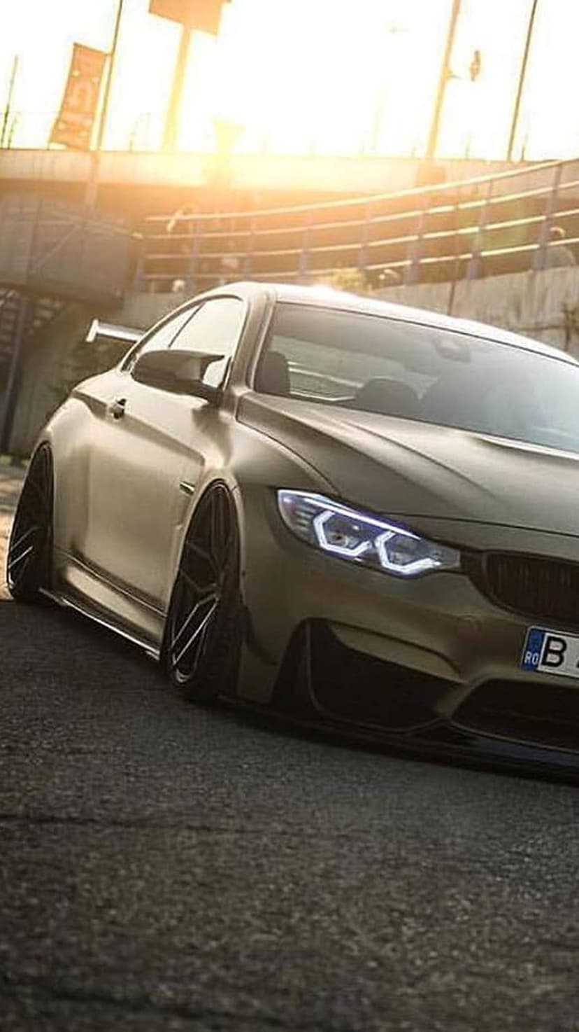 BMW M4 coupe with golden matte paint, widebody kit, and glowing LED headlights parked at a low-angle stance.