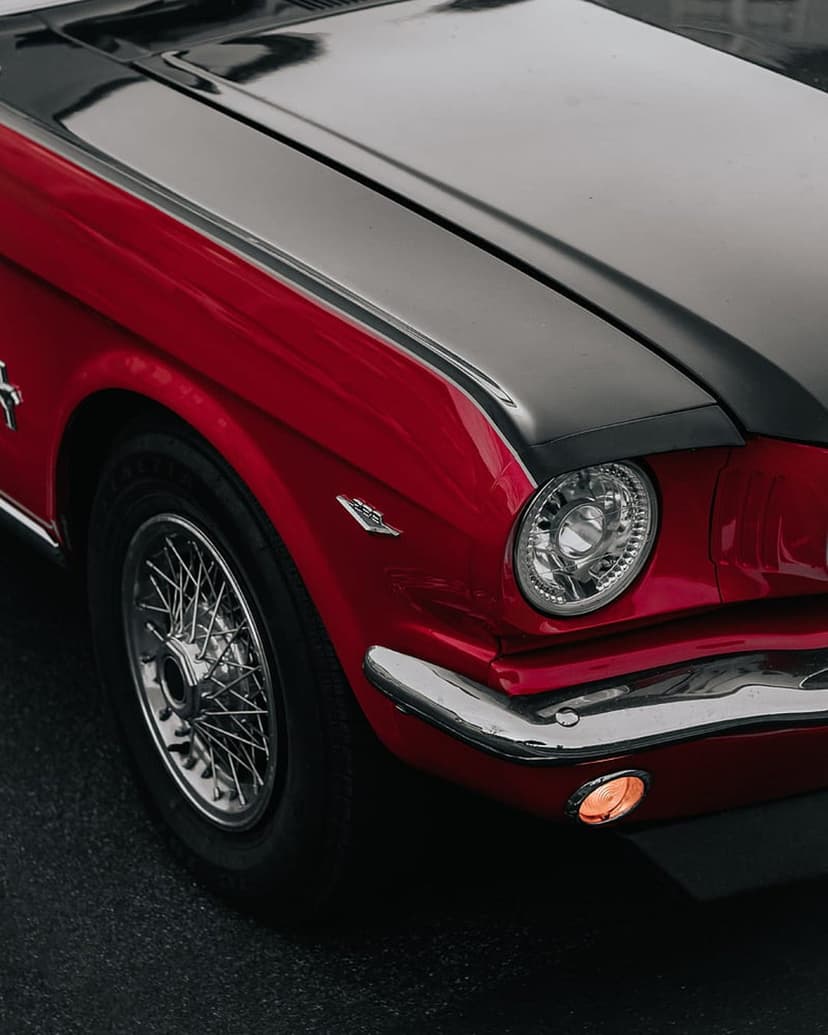 Red Ford Mustang front profile with a black hood, wire wheels, and a chrome bumper with glowing amber lights.