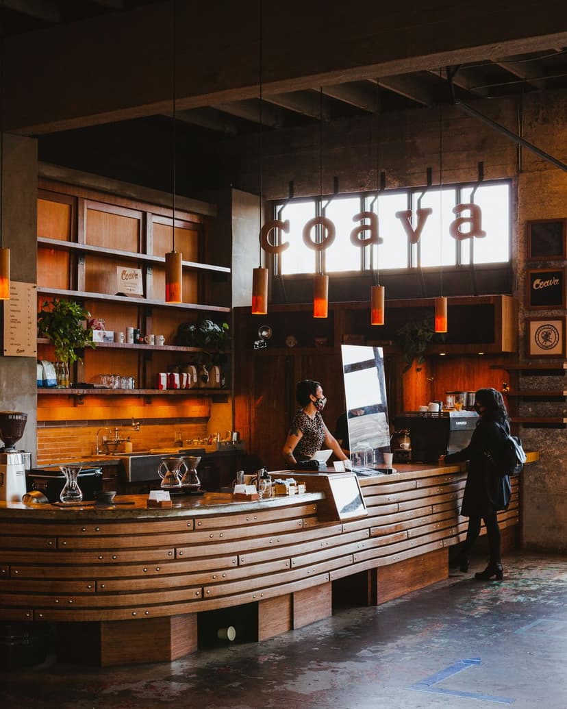 Curved wooden coffee bar with an illuminated coava sign and glowing orange pendant lights in a modern cafe.