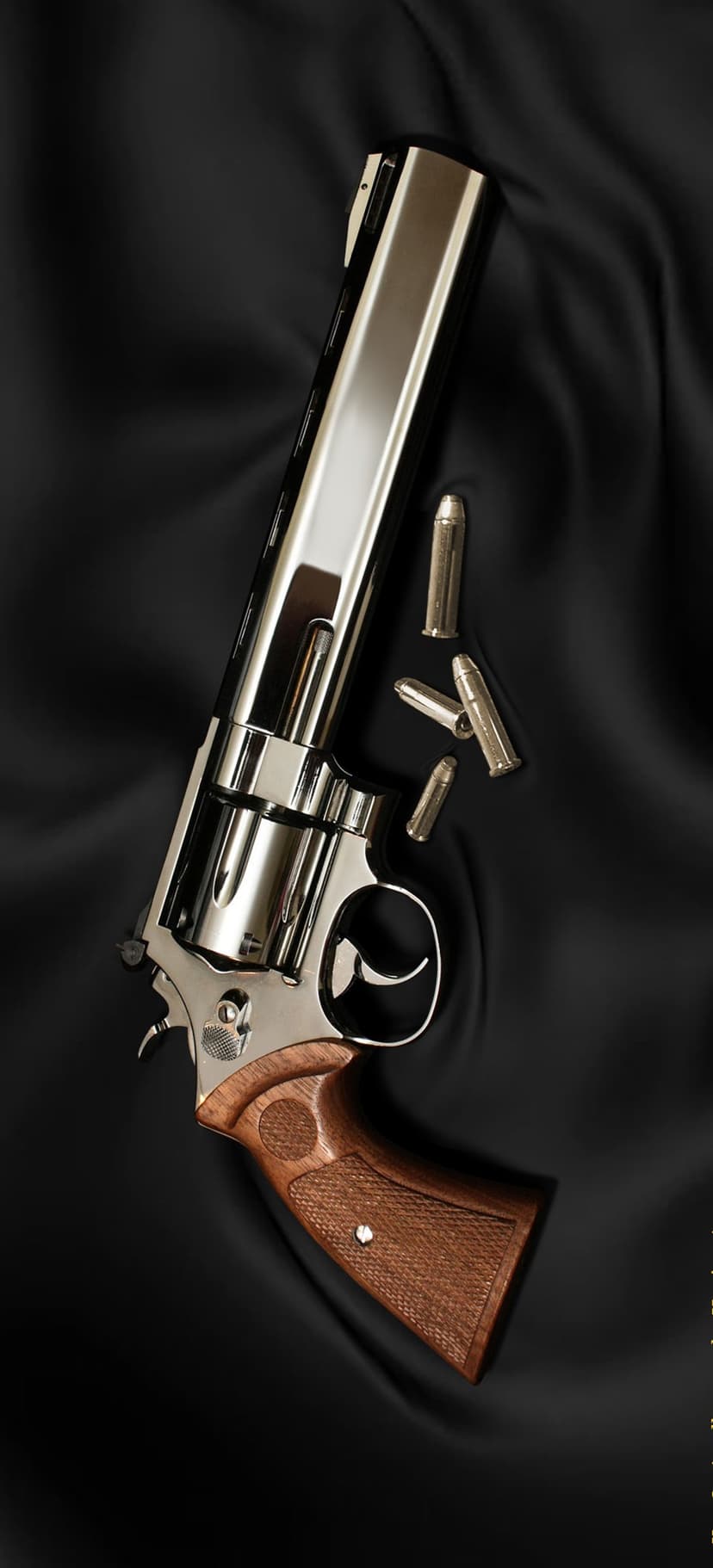 Silver revolver with a wooden grip rests on folded black silk next to three brass bullets in a vertical layout.
